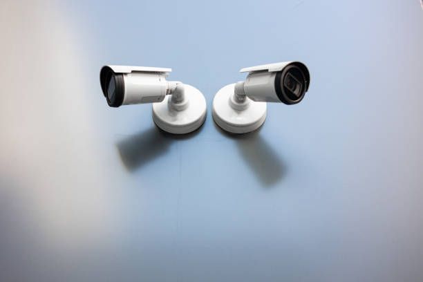 Two white security cameras are mounted on a light blue wall.