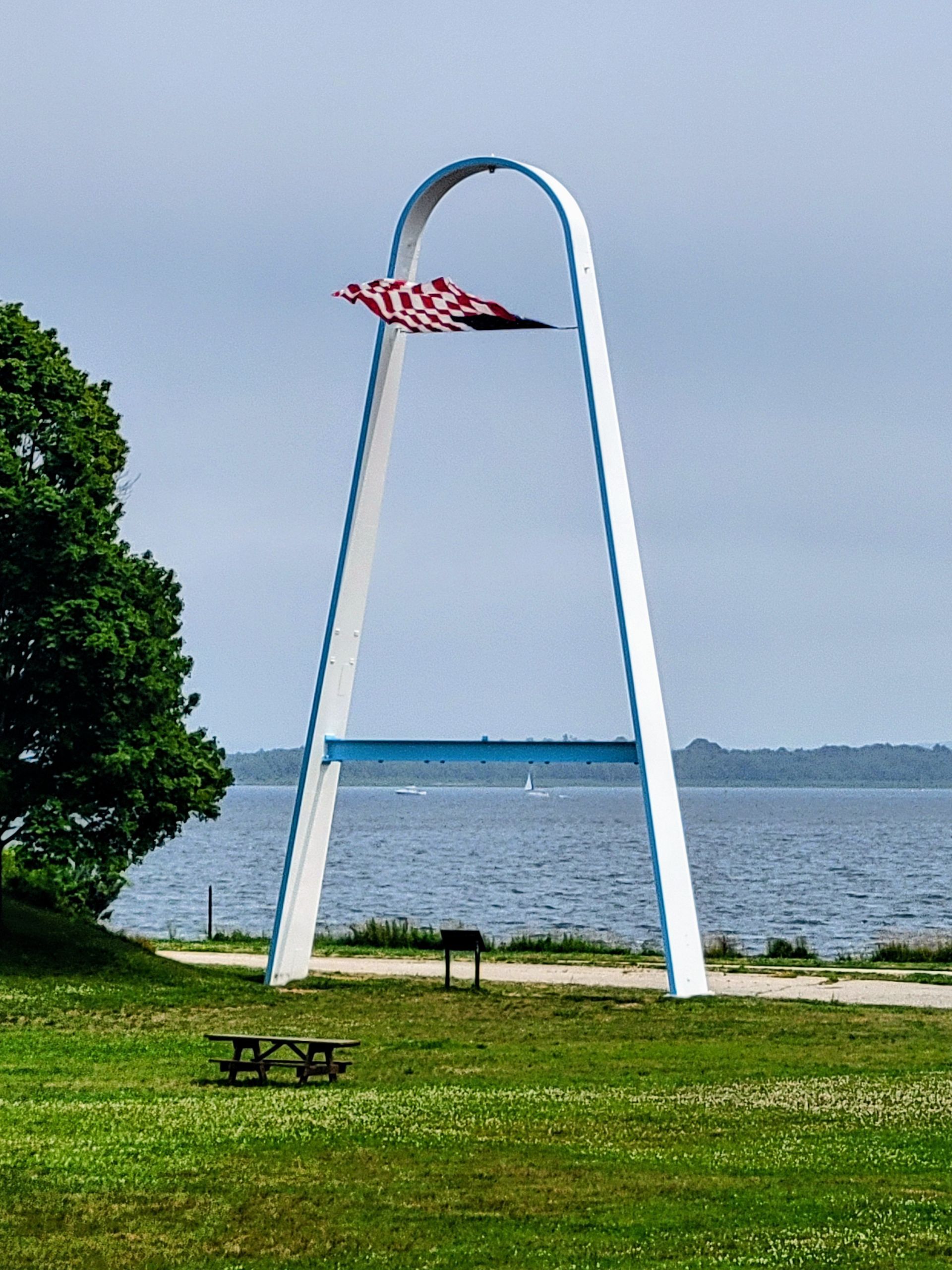 White arch monument with a red and white flag, on a grassy waterfront.