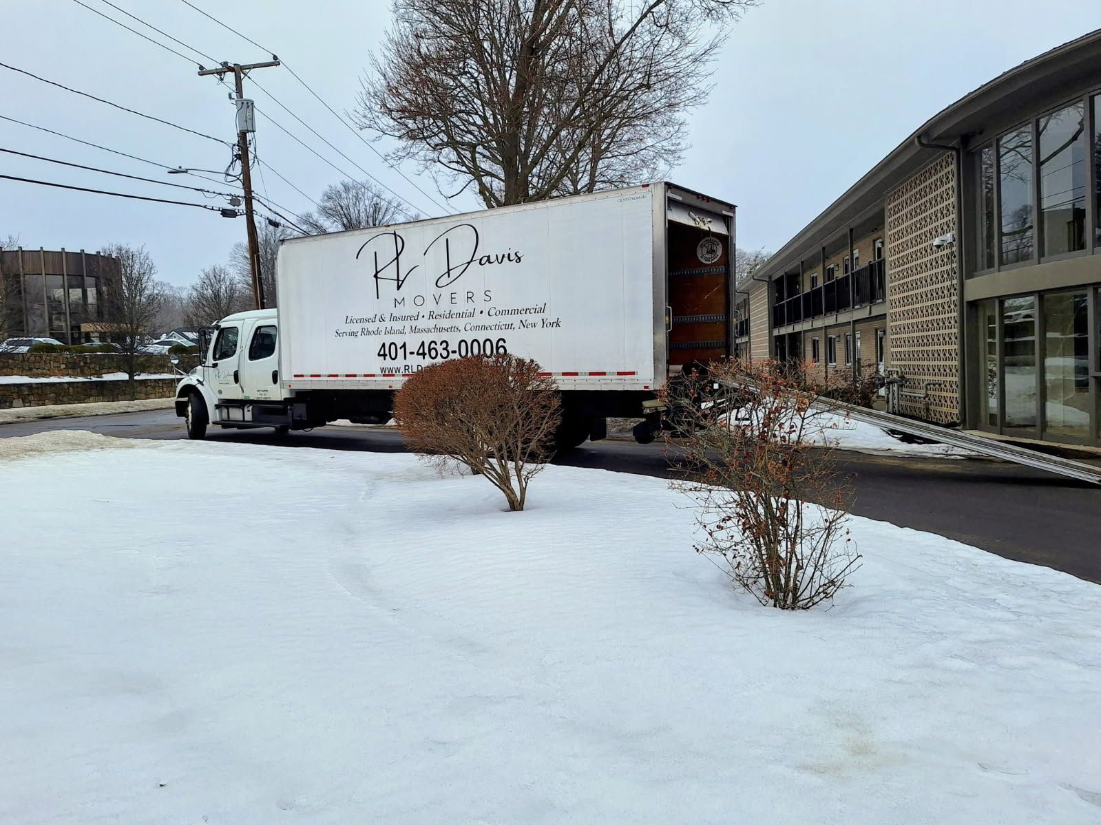 White moving truck parked in front of a building with a snow-covered lawn.