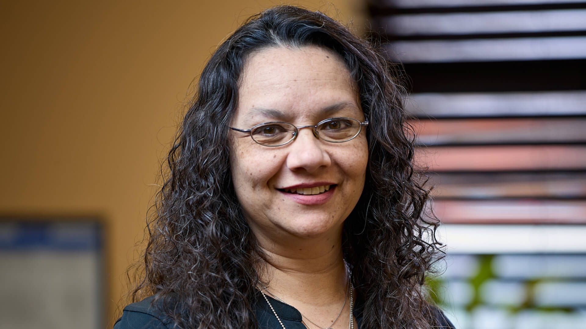 a woman with curly hair and glasses is smiling for the camera .