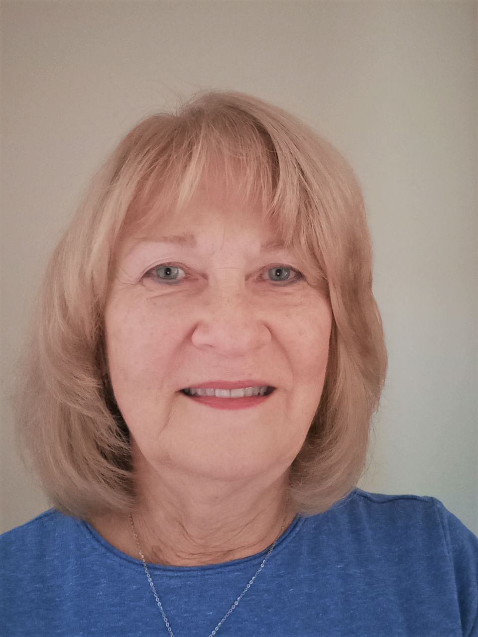 Woman with blonde hair smiling, wearing a blue shirt.
