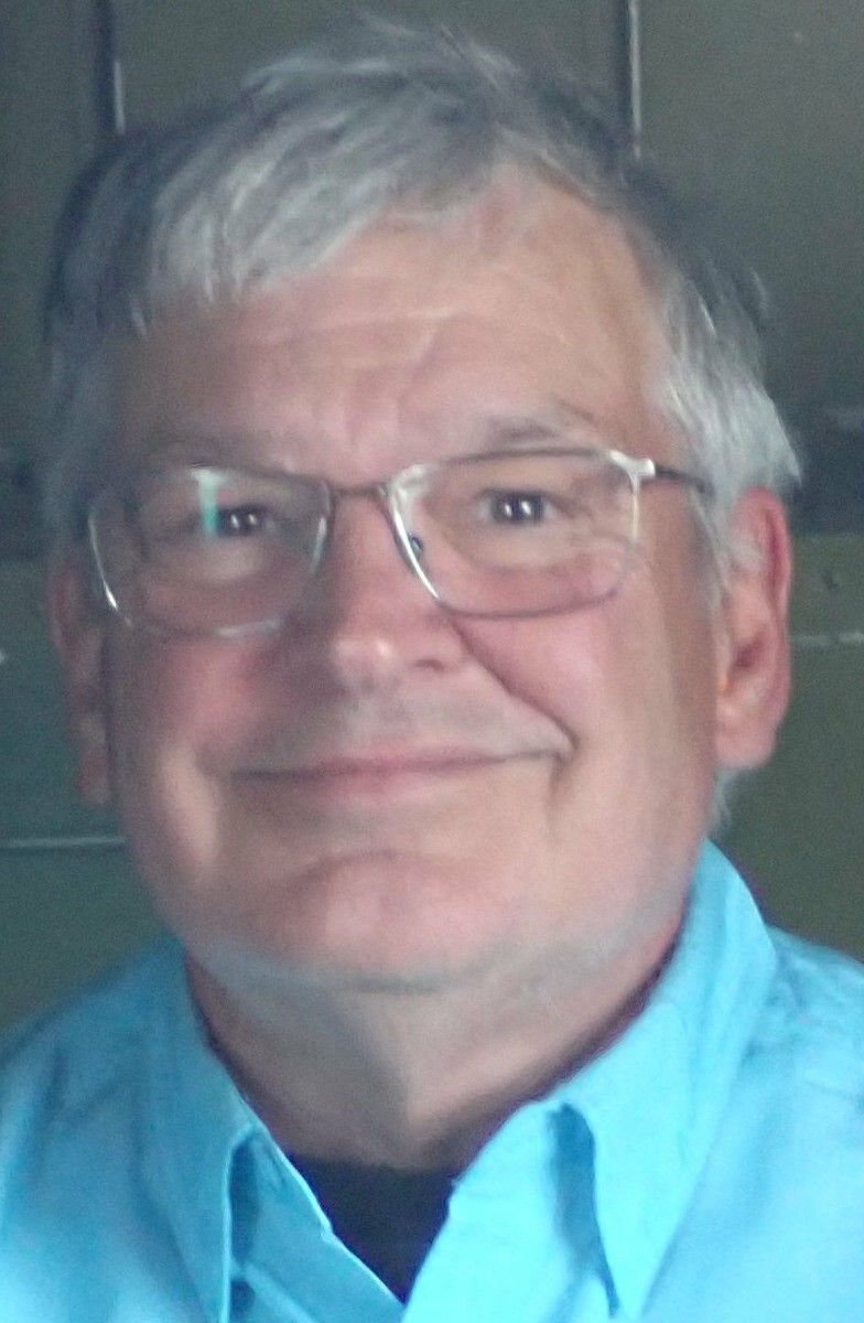 Man with glasses, graying hair, and light blue shirt smiles at the camera.