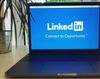 Laptop displaying the LinkedIn logo: blue background, white text, in a brightly lit room.