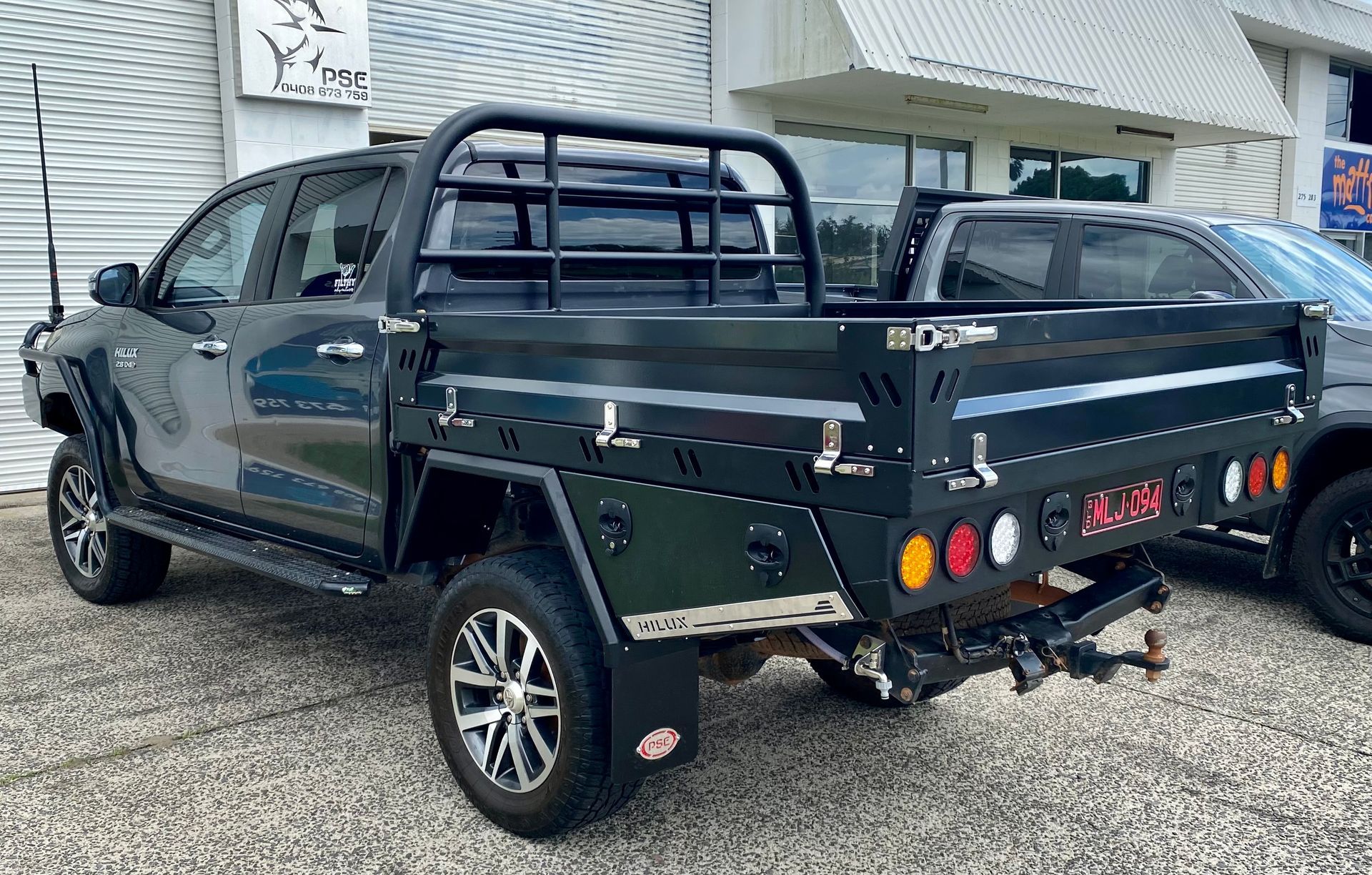 A black truck with a trailer attached to it is parked in front of a building  — PSE Stainless Steel Fabrications in Manunda, QLD