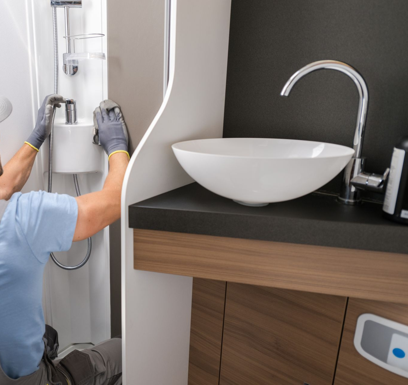 Person in gloves fixing shower, next to a sink in a modern bathroom.