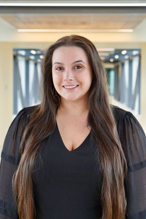 A woman with long hair is wearing a black shirt and smiling for the camera.