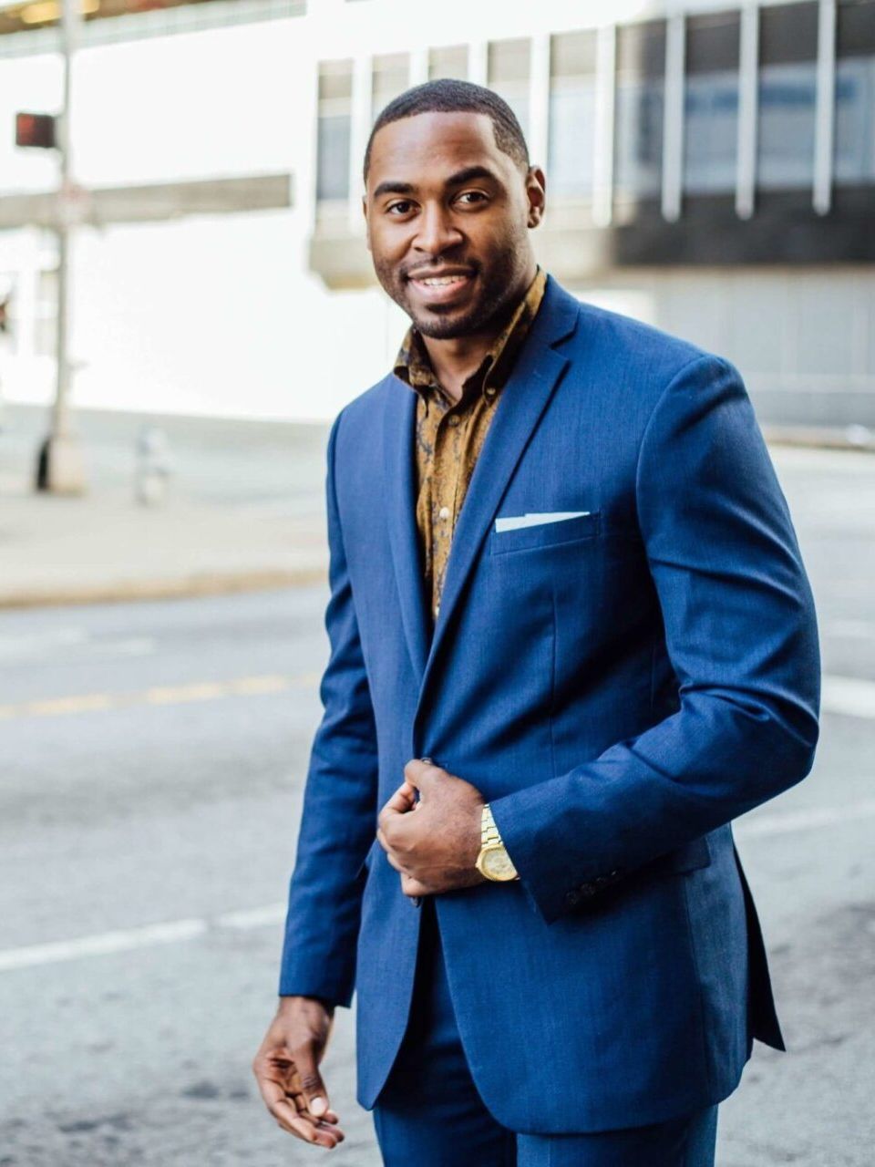 A man in a blue suit is standing in front of a building.