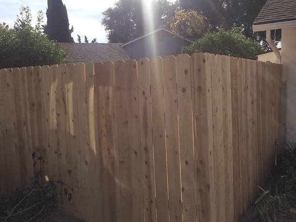 Wooden fence in a backyard setting, angled corner, with sun shining through.
