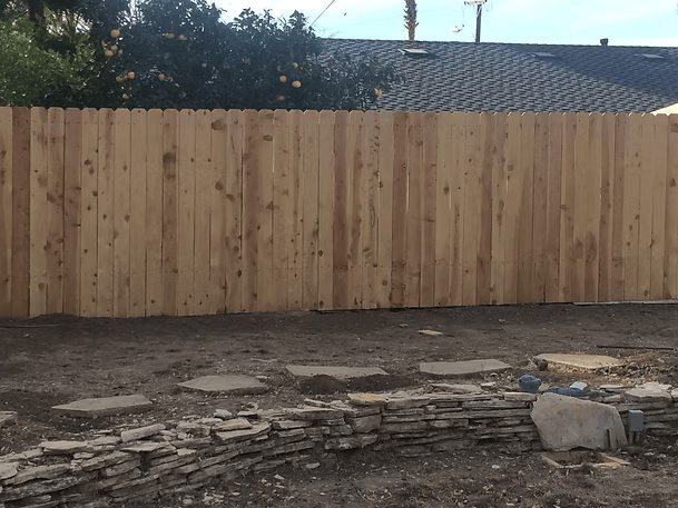 Wooden fence in backyard with stone path and retaining wall.