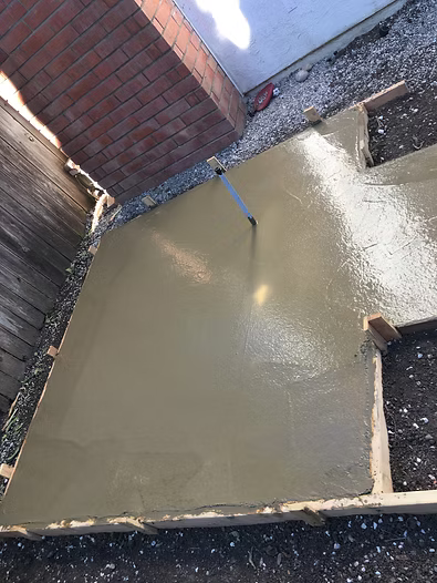 Freshly poured concrete patio with a vibrator, next to a brick structure and wooden forms.