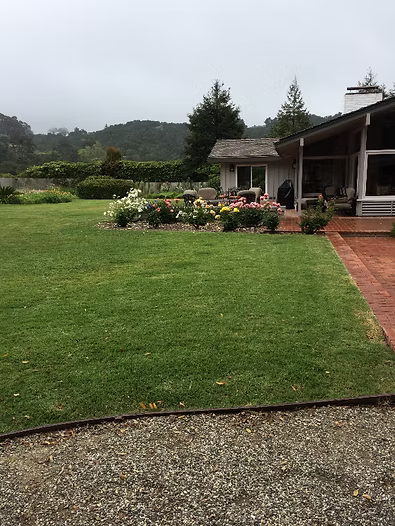 A green lawn in front of a house with flowers and a cloudy sky.