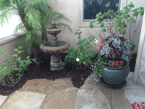 A stone fountain and potted plants in a shaded courtyard.