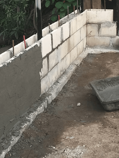 Brick wall under construction, with gray cement being applied. A tray of cement sits nearby.