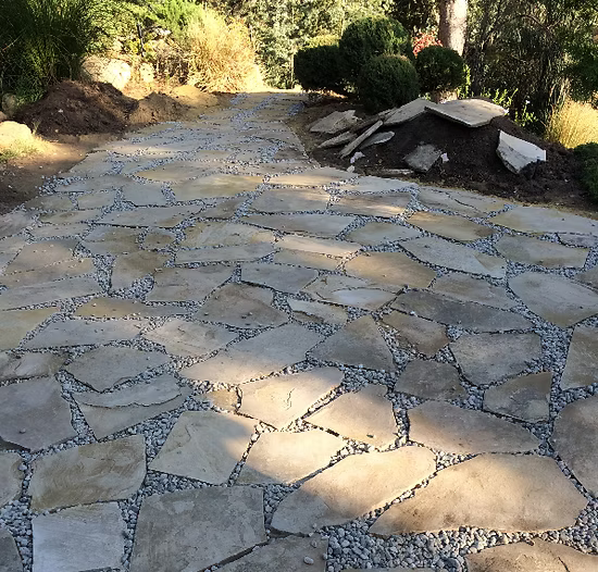 Stone path with irregularly shaped slabs and gravel, leading uphill in a garden setting.