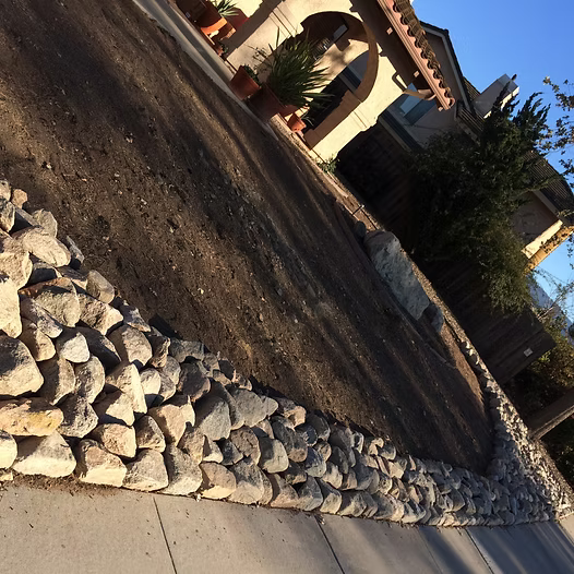 Rock border along a driveway, with dirt bed and house in the background.