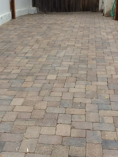 Brown and gray brick pavers cover a driveway or patio area, leading to a wooden fence.