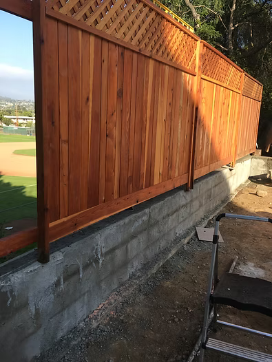 Wooden fence with lattice top, built on a concrete wall, overlooking a baseball field.