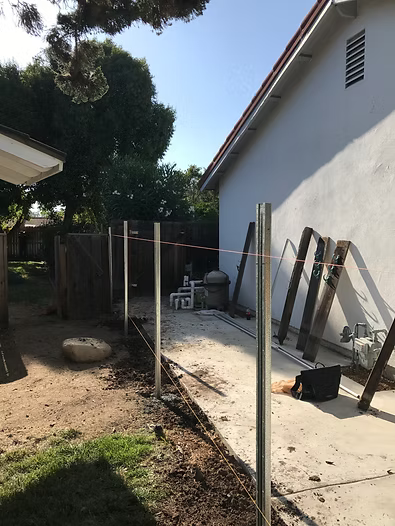Backyard with a partially built fence, next to a house.