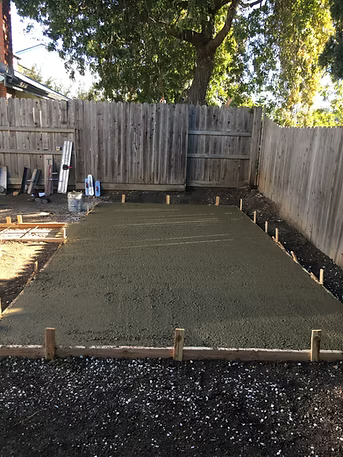 Freshly poured concrete slab in a backyard, surrounded by wooden forms and a wooden fence.