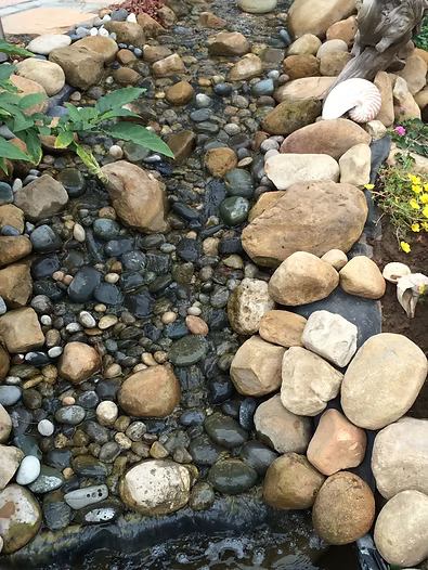 A rocky stream bed with water flowing, surrounded by various sized stones.