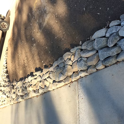 Rocks lining a concrete wall, with shadows overhead.