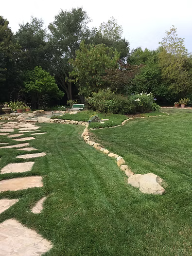 Stone path and manicured lawn leading to garden with trees.