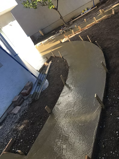 Wet concrete pathway being poured in a yard, with wooden forms and tools visible.