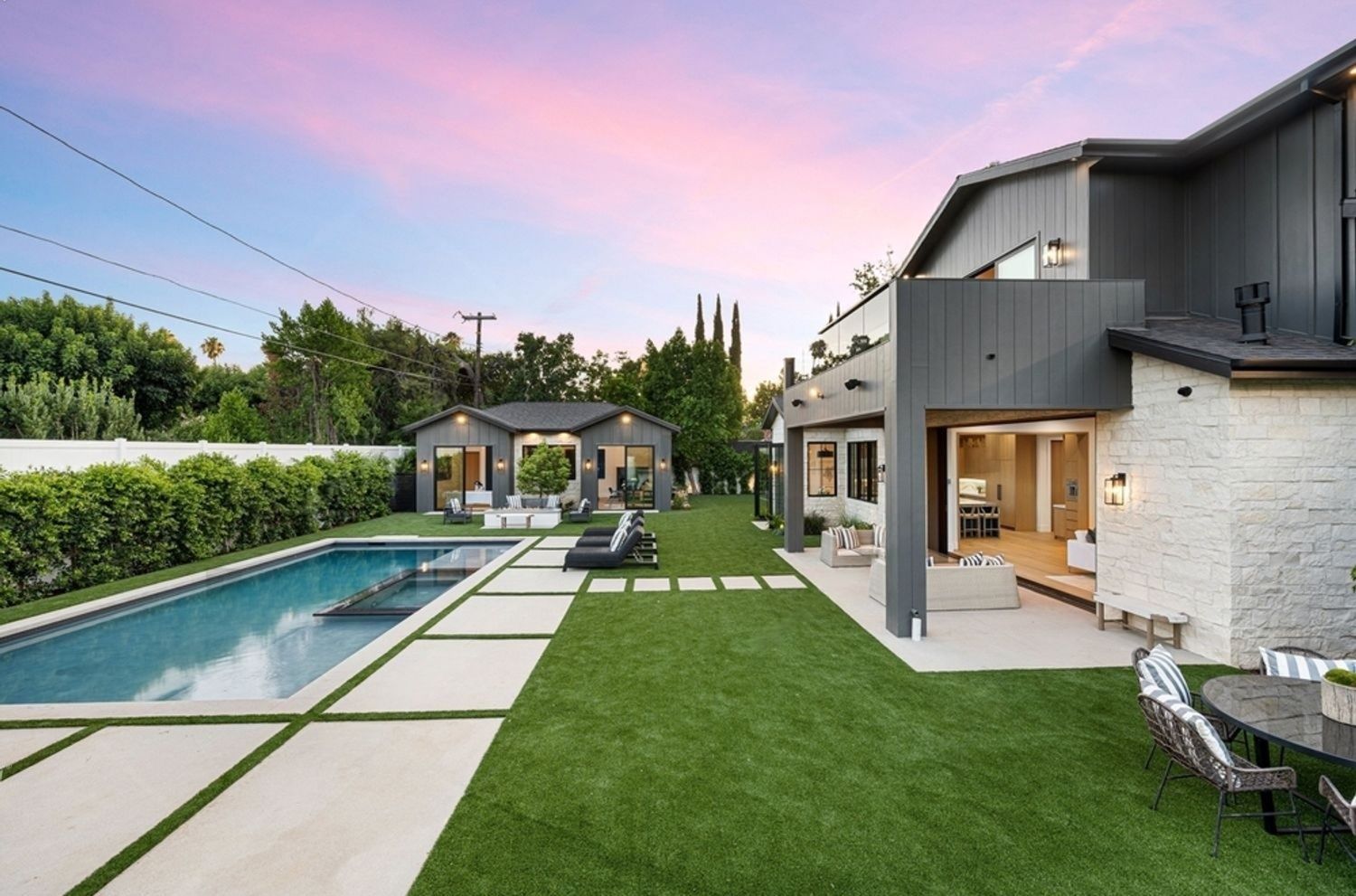 Luxury home exterior with pool, lawn, and outdoor seating under a pink and blue sunset.