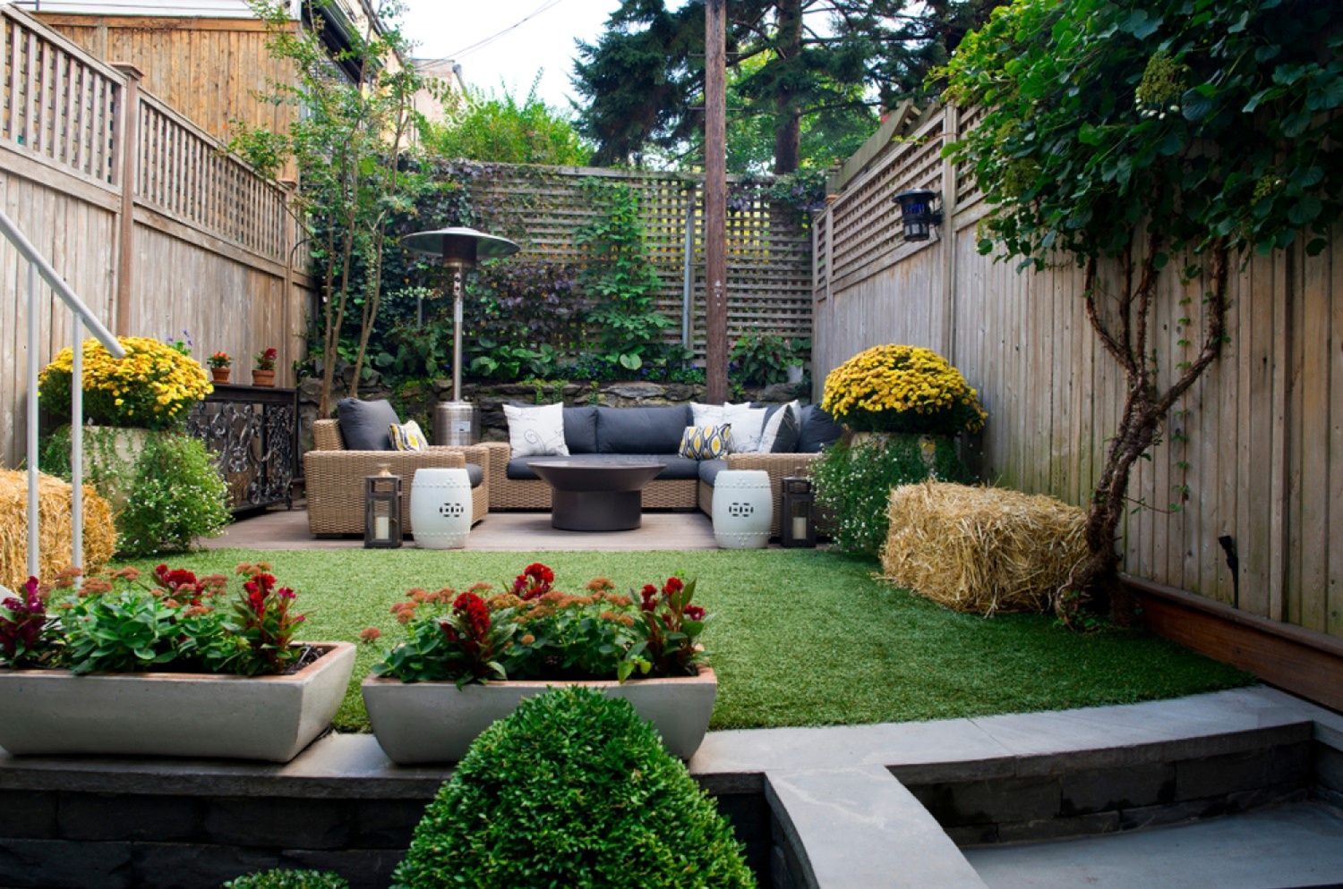 Cozy backyard patio with outdoor furniture, a small lawn, and flower planters between wooden fences.