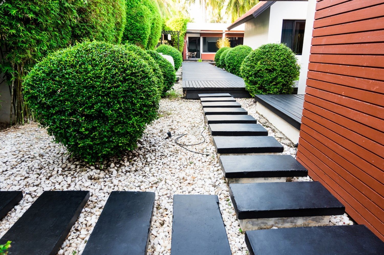 Stone pathway through garden with round green bushes and white pebbles.