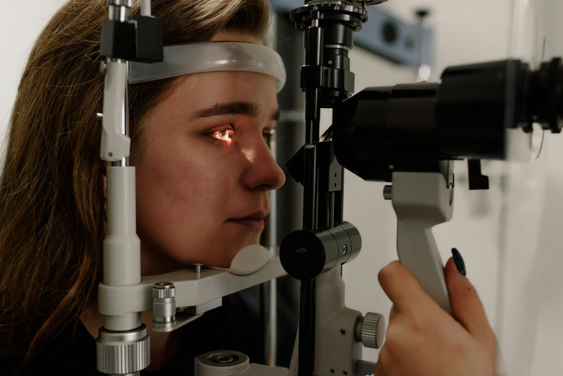 Woman undergoing an eye exam with a slit lamp machine, eye illuminated.