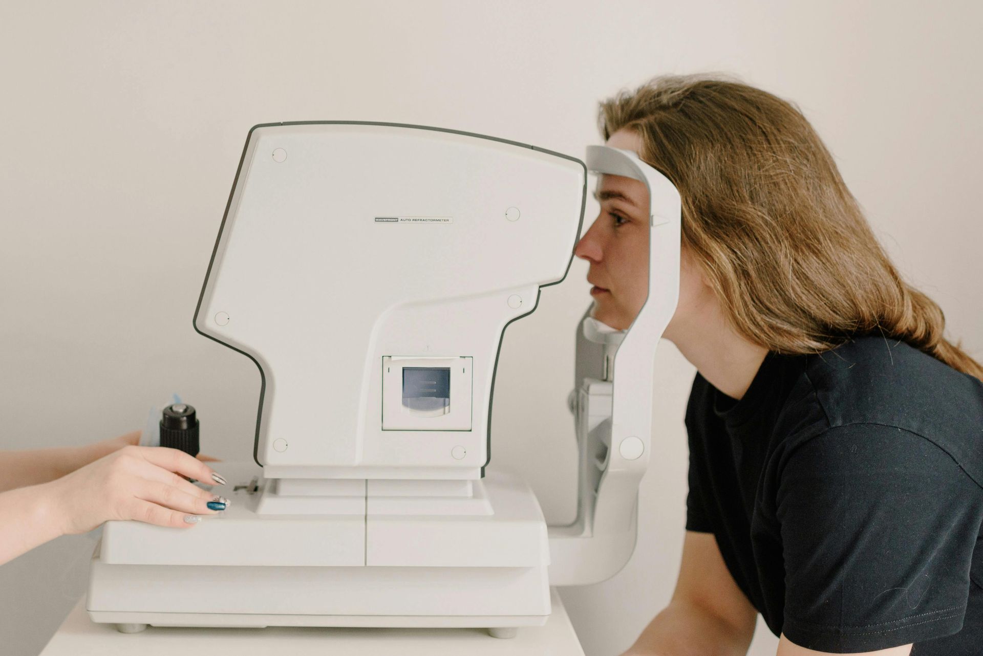 Person undergoing eye exam using an autorefractor. White machine with chin rest, a person seated.