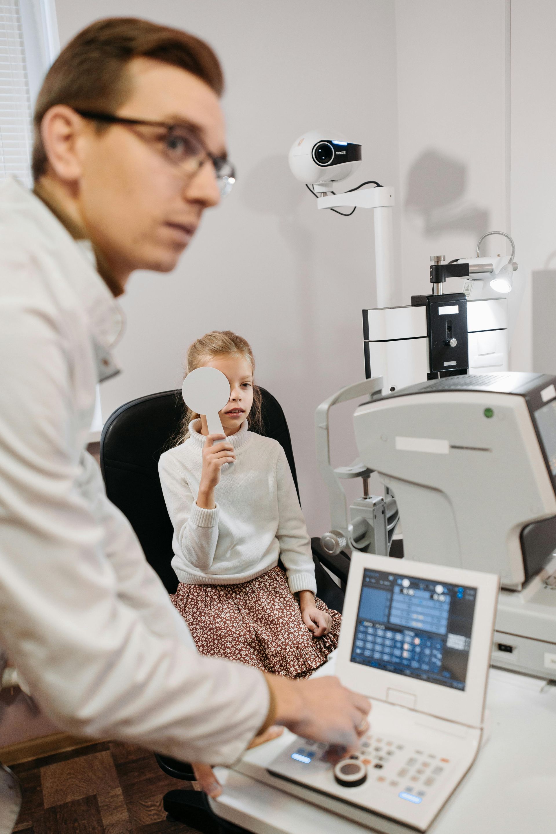 Optometrist examining a child's eyes with a machine in an office setting.