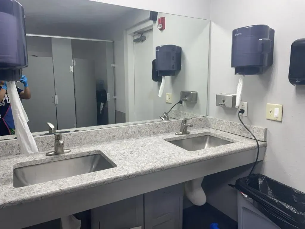 Bathroom with two sinks, paper towel dispensers, mirror, and a trash can.