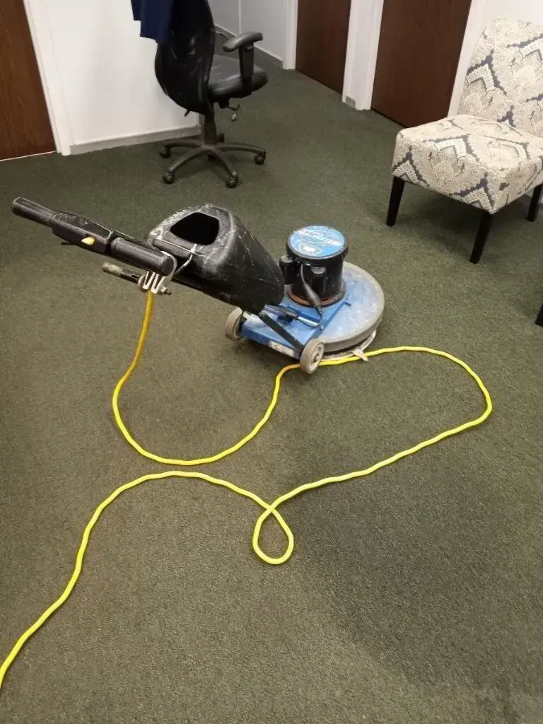 Floor buffer on green carpet in an office, with a chair and office chair in the background.