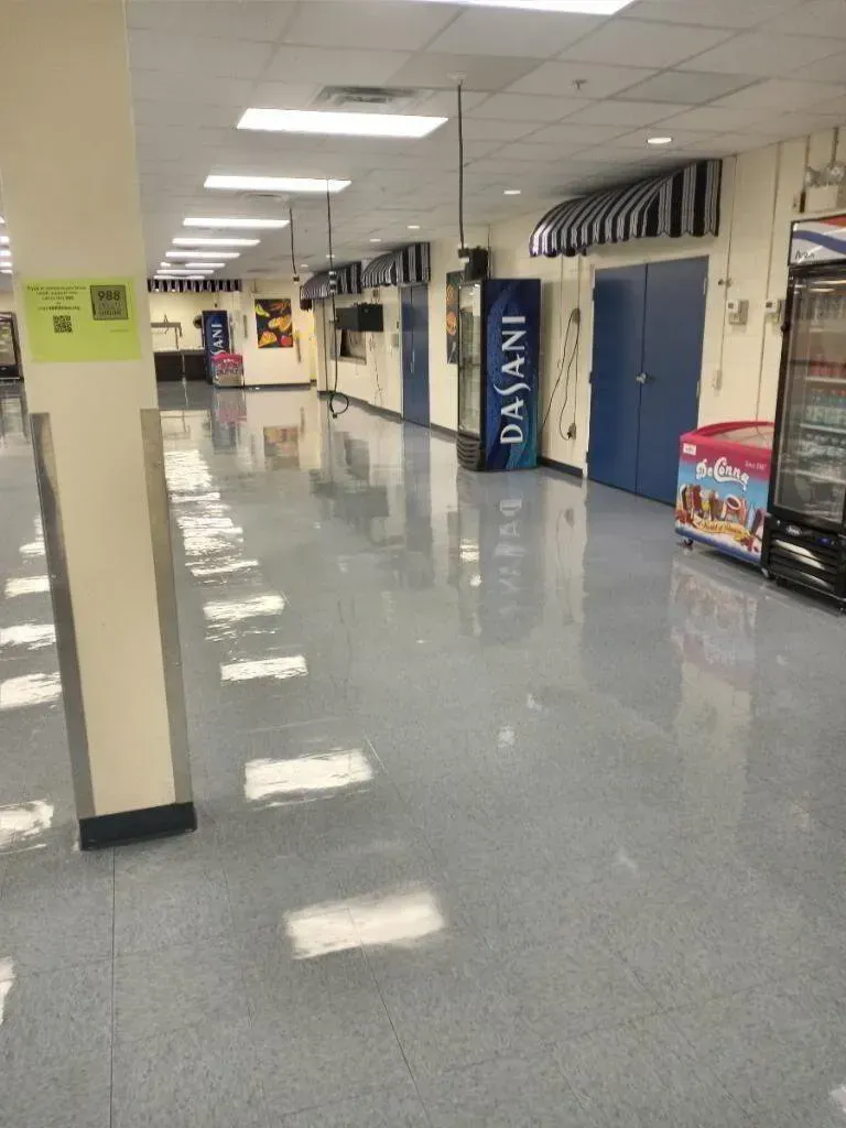 Hallway with shiny gray floor, vending machines, blue doors, and a striped awning.