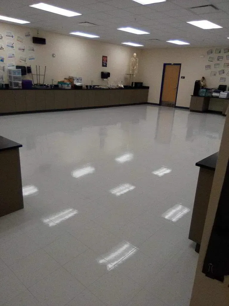 Empty science classroom with shiny floor, lab tables, and a skeleton, illuminated by ceiling lights.