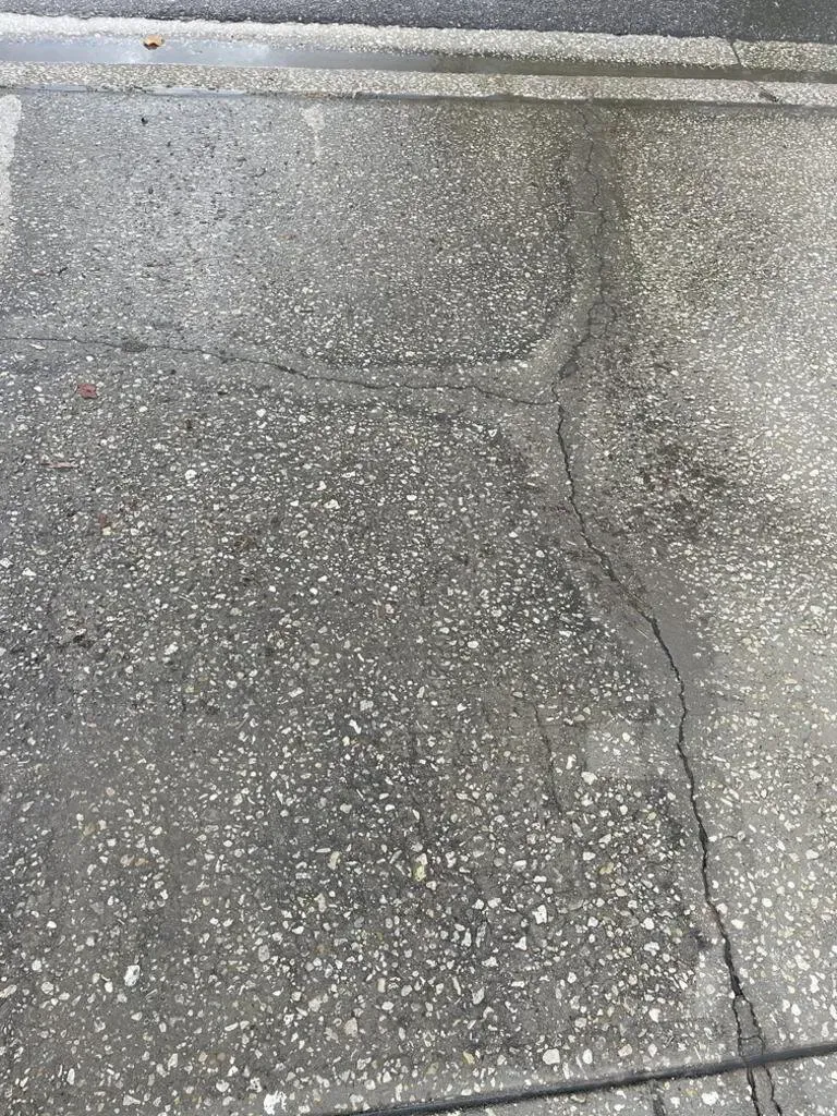 Cracked concrete surface, dark gray with white speckles. Vertical crack across the center, some water visible.