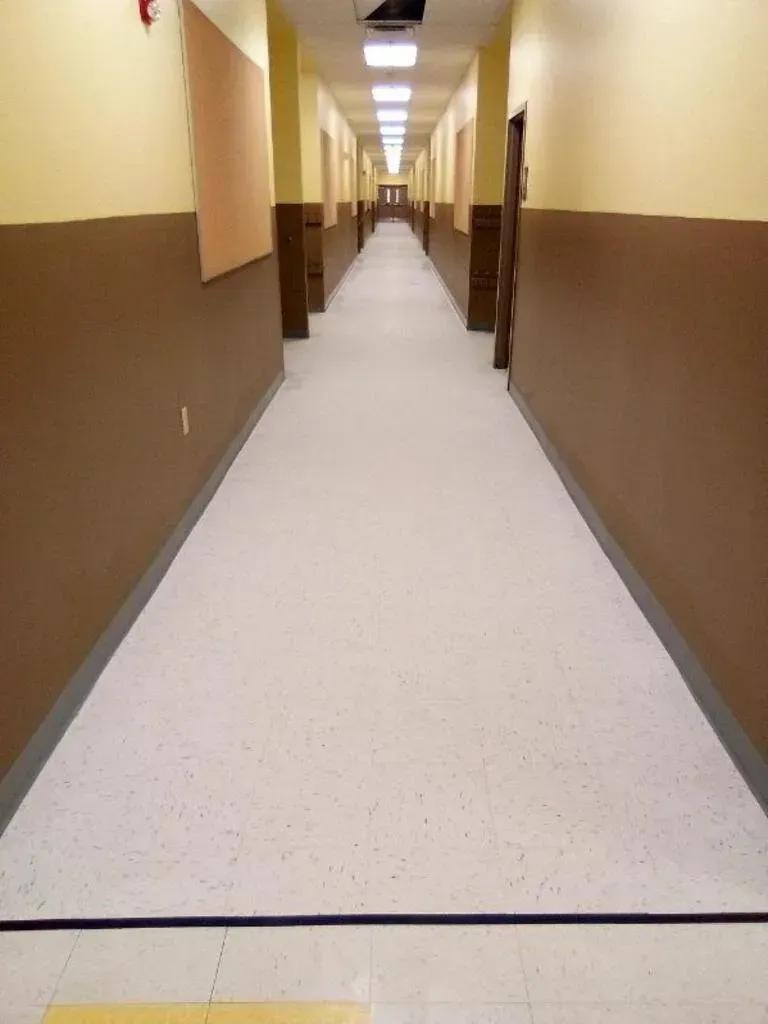 Long, empty hallway with brown and beige walls, beige floor, and doors along both sides.