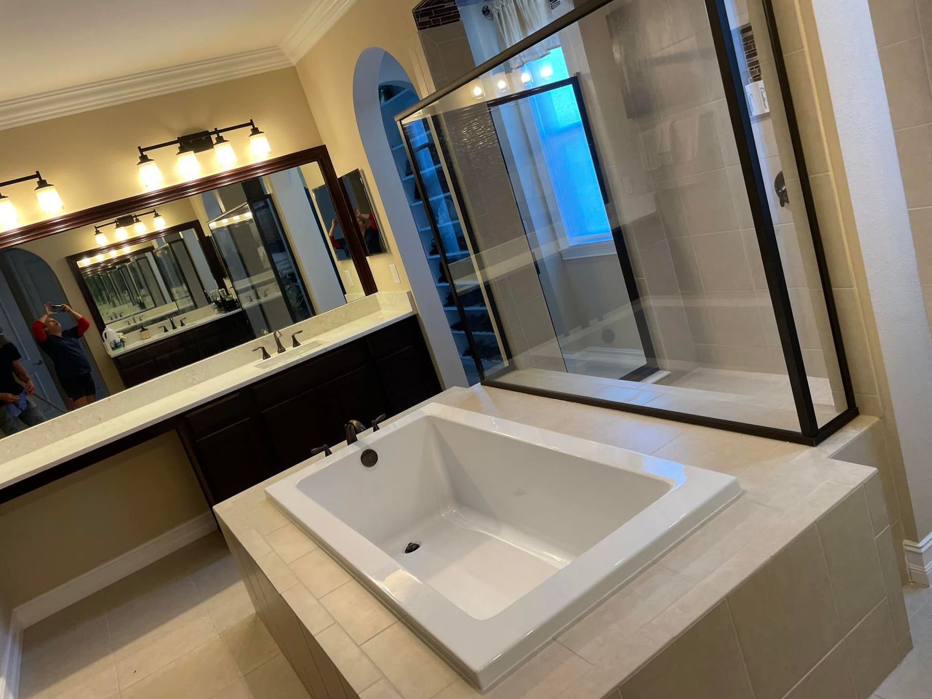 A luxurious bathroom with a white tub, glass shower, dark vanity, and large mirrors.