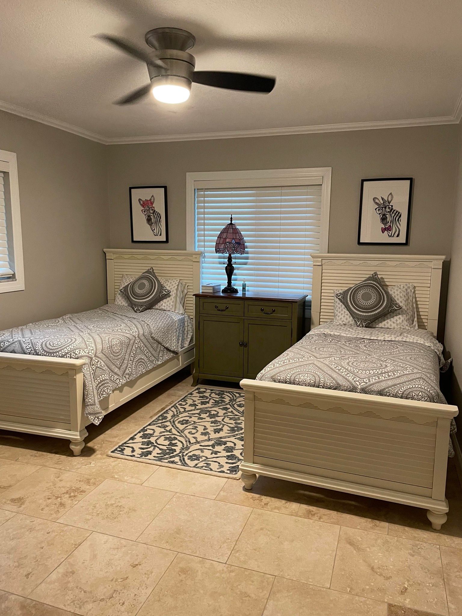 Two twin beds in a bedroom with neutral walls, a rug, and a dresser between the beds.