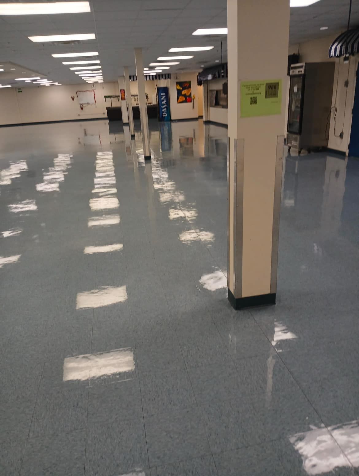 Blue-floored, empty room with bright overhead lights reflecting. Beige support pillars.
