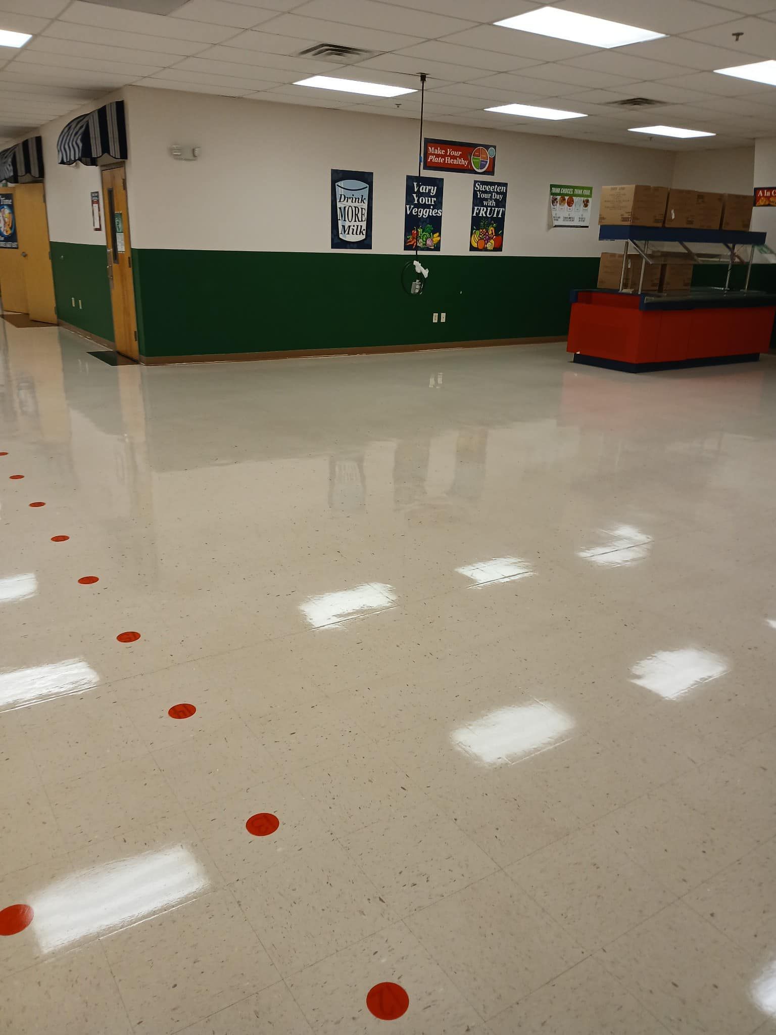 Empty cafeteria with shiny floor. Red dots and white squares mark the floor. Green and white walls, serving counter.