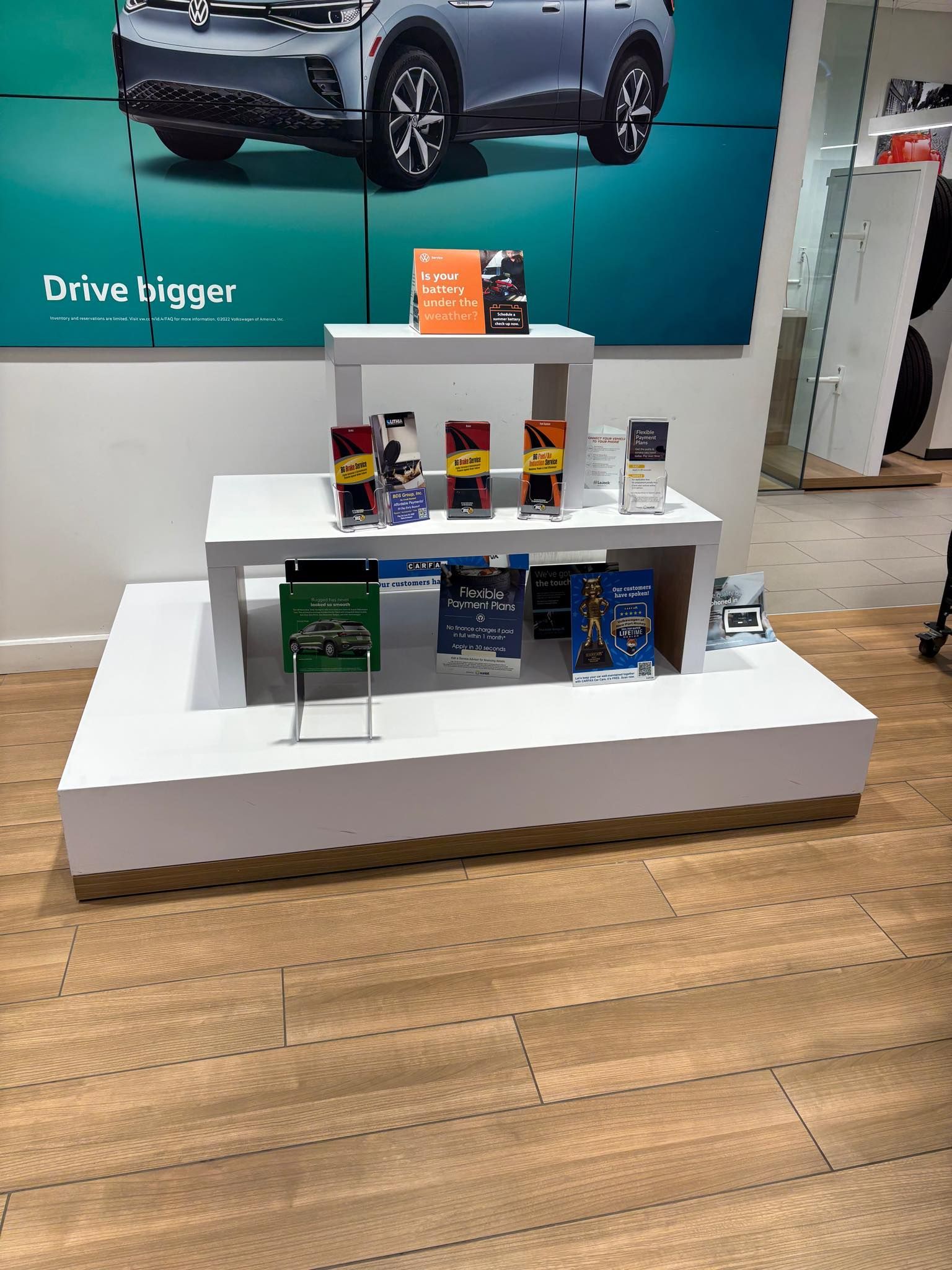 Display stand with car brochures in a showroom, beneath a large vehicle advertisement.