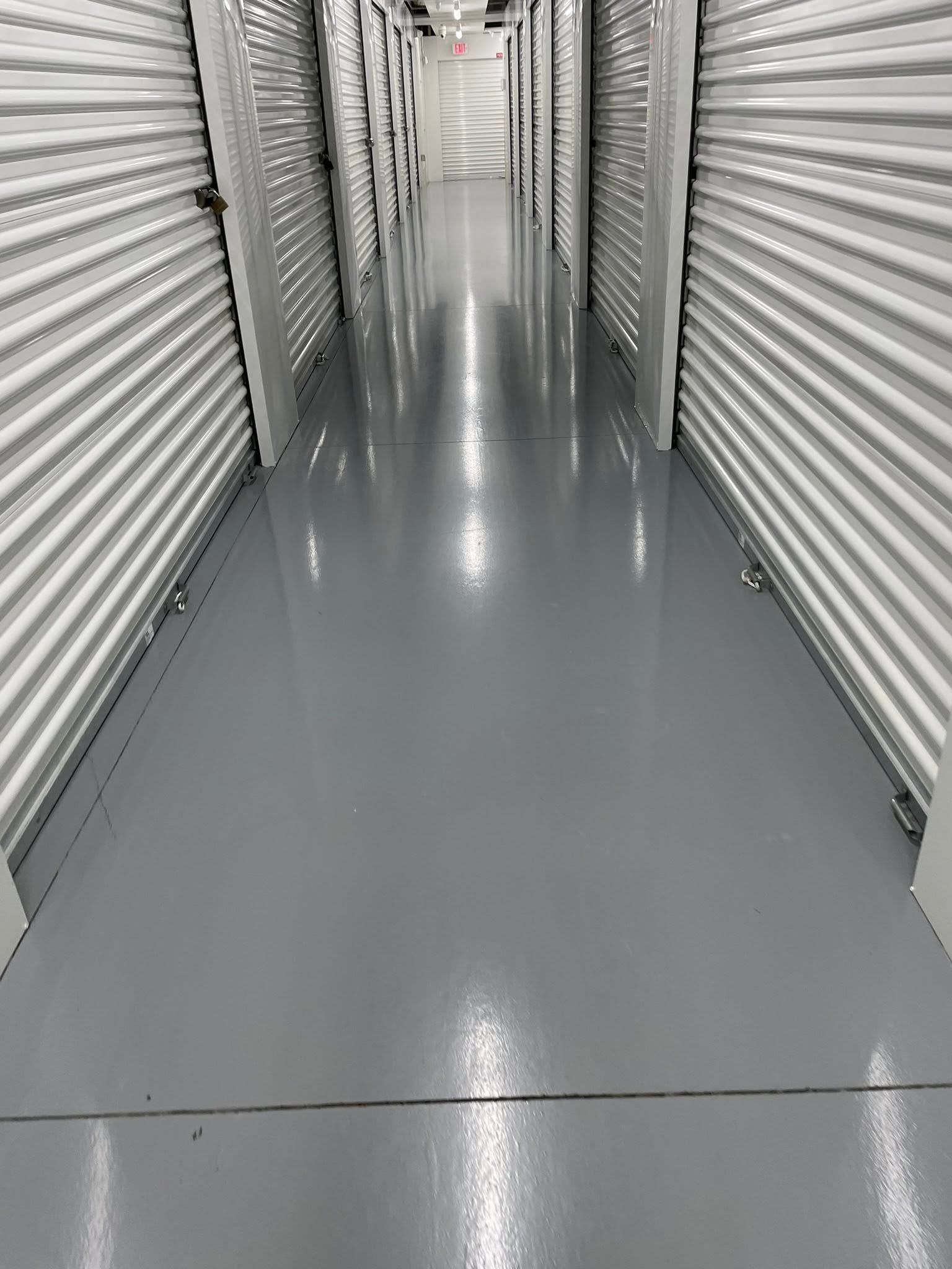 Long, gray storage unit hallway with units on both sides, illuminated overhead lighting.