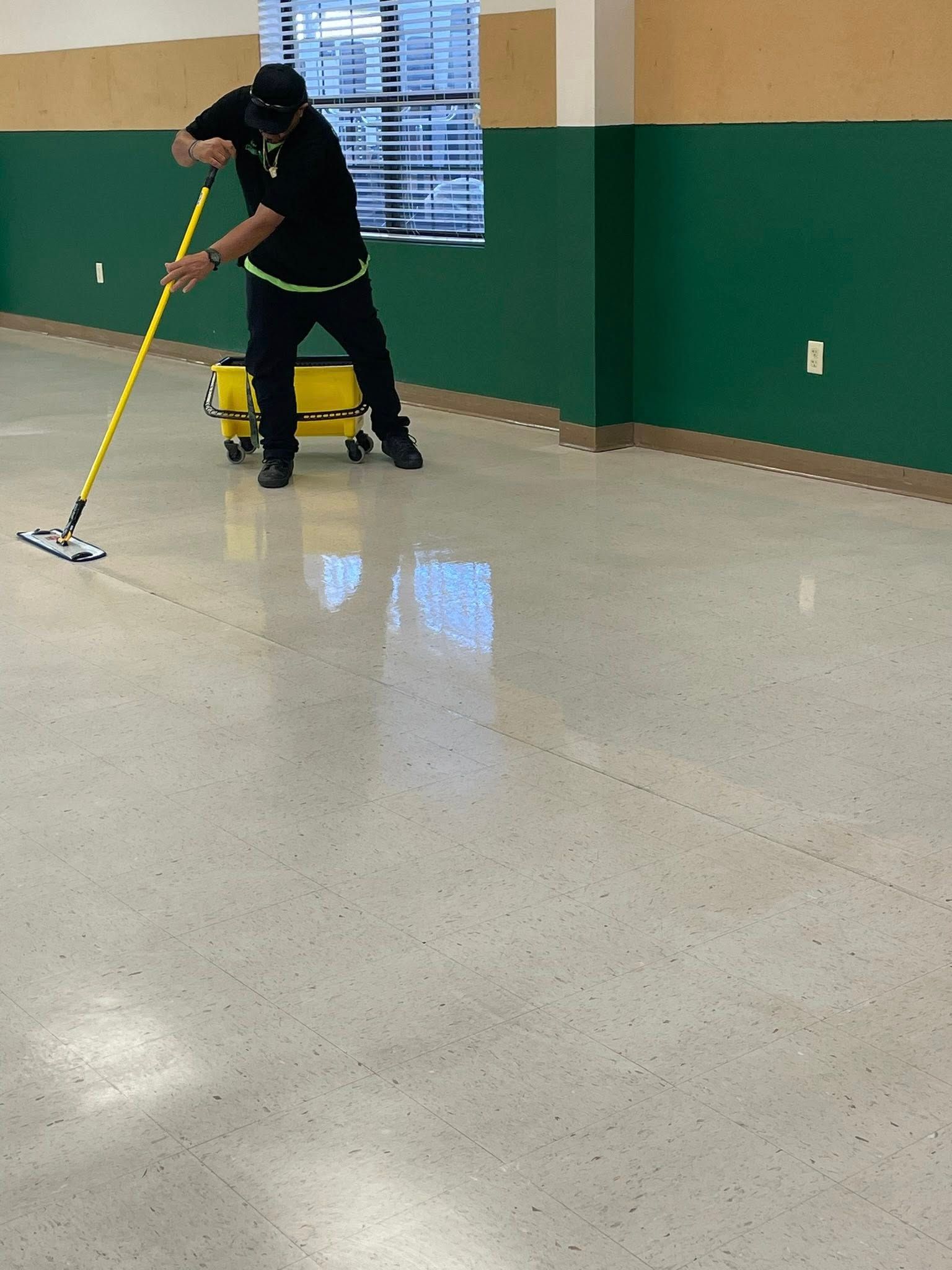 Person mopping a shiny, speckled floor in a room with green walls.