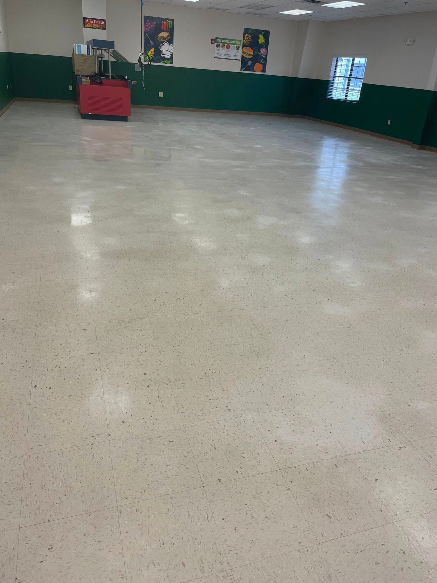 Empty room with shiny beige floor, green wainscoting, and posters on white walls. Red cart in the background.
