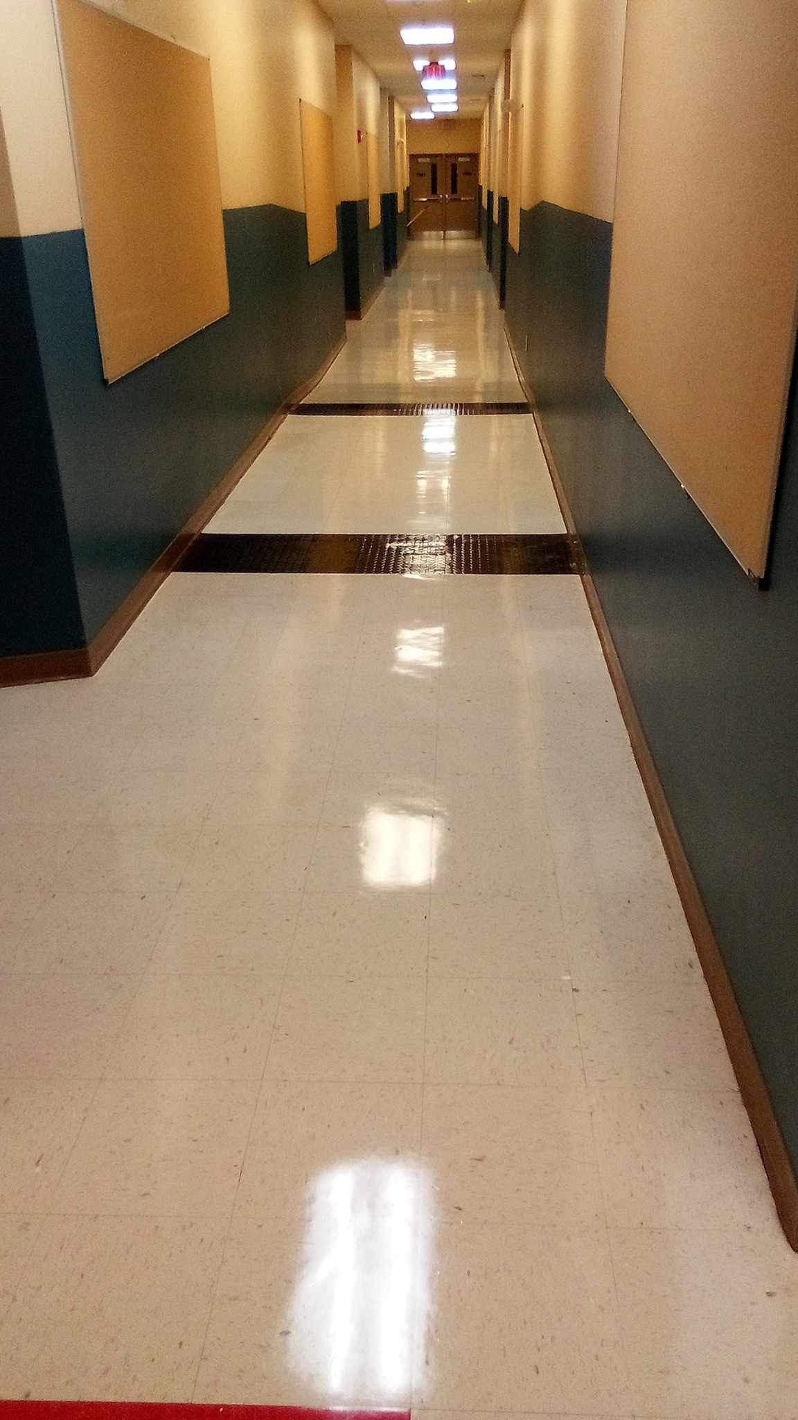 Long school hallway with light-colored floor, tan walls with dark blue accents.