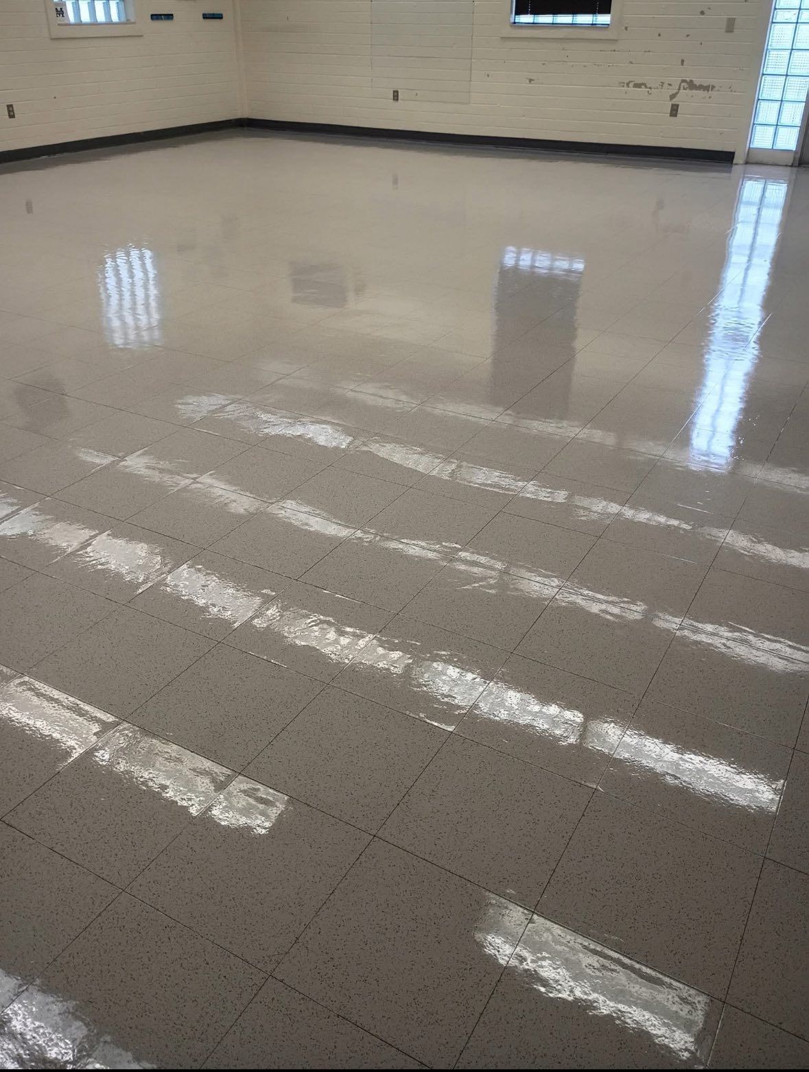 Shiny tiled floor reflecting sunlight from barred windows in a mostly empty room.