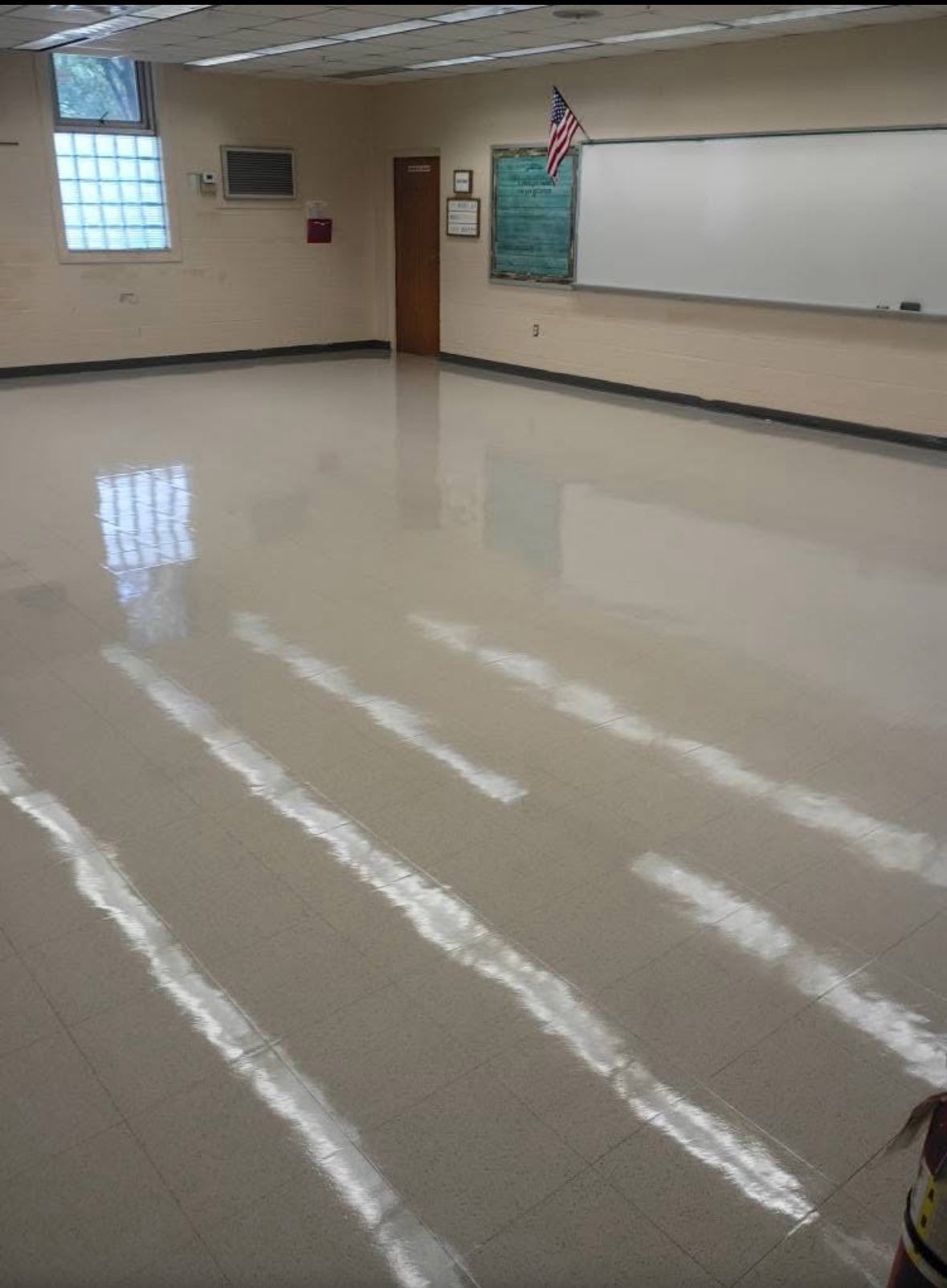 Empty classroom with a shiny, light-colored floor, a whiteboard, and a window.